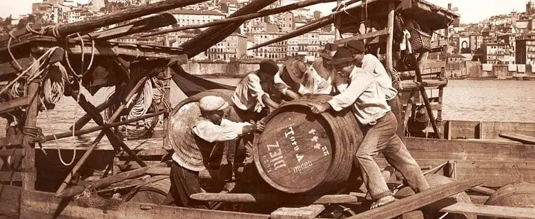 Imagem de ambiente histórico com barricas e trabalhadores ligados ao vinho